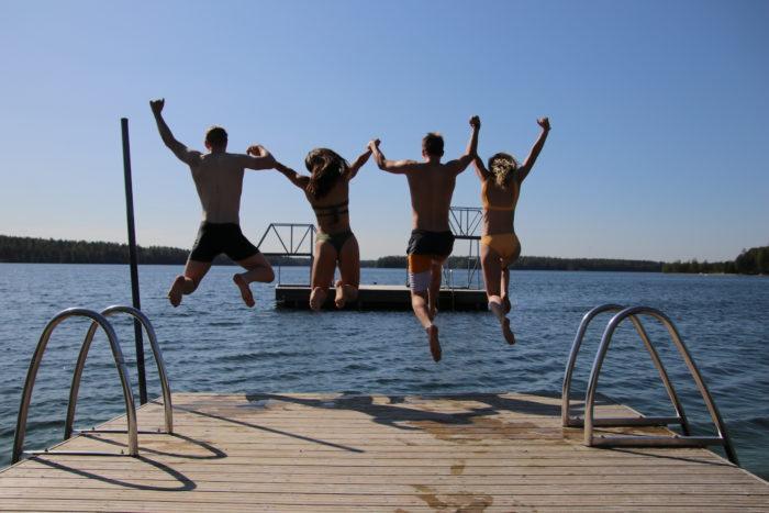 Neljä nuorta hyppää käsikädessä laiturilta Sääksjärveen.