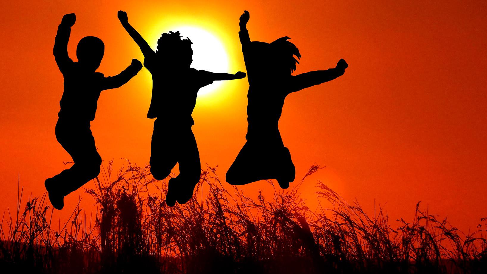 Hyppäävien nuorten silhuetit laskevan auringon edessä