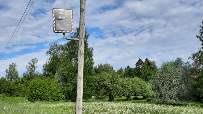 Nopeusnäyttötaulu pylväässä vihreän kesäisessä peltomaisemassa.