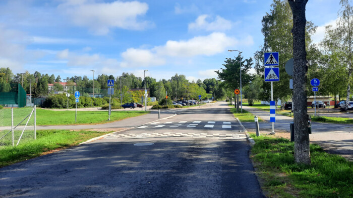 Katu, pysäköityjä autoja ja liikennemerkki, jossa kerrotaan suojatiestä ja pyöräilijän ylityspaikasta suojatien vieressä Kuntotiellä Klaukkalassa.