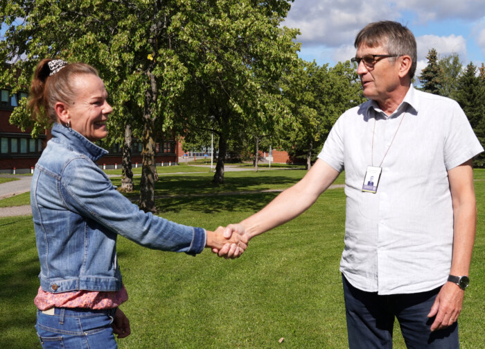 Uusi maankäyttöpäällikkö Tarja Kariniemi ja eläkkeelle jäänyt Hannu Kujala kättelevät kunnanviraston edessä olevalla nurmialueella.