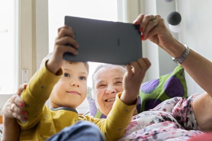 Hymyilevät isoäiti ja pieni poika katsovat yhdessä tablettia.
