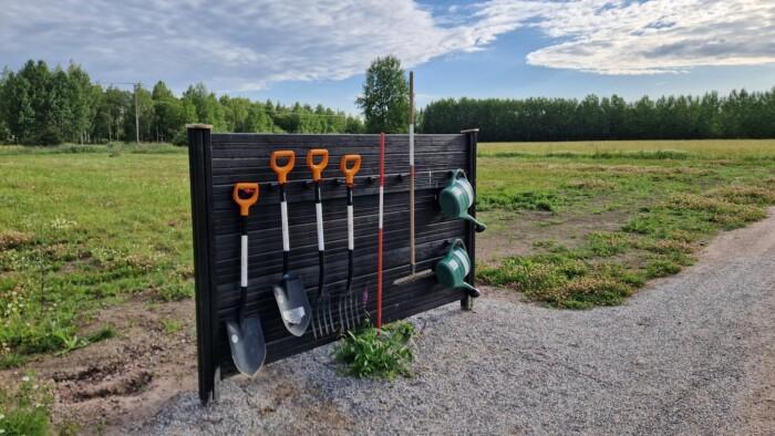Puutarhatyäkaluja, kuten lapioita ja haroja, kiinnitettynä telineeseen viljelyspalsta-alueella.